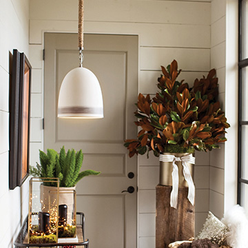 white rustic farmhouse pendant hanging in an entryway over a wood side table with ferns and twinkle lights