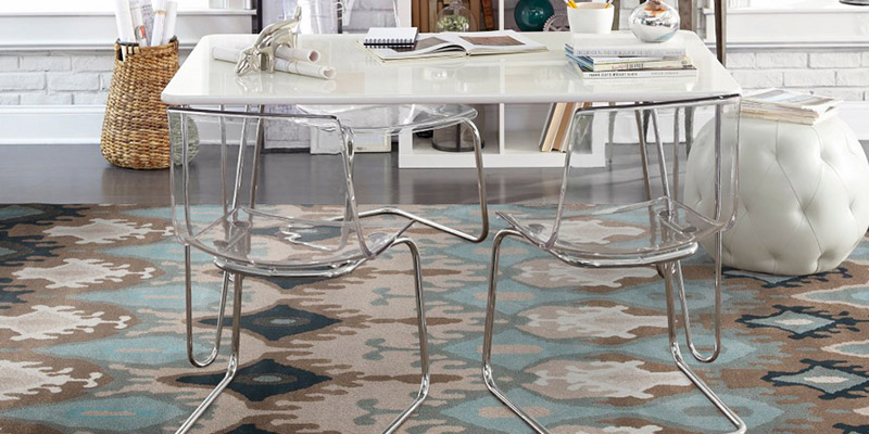 how to choose an area rug - a colorful, artistic rug under a modern acrylic table with clear acrylic chairs, and a white leather ottoman