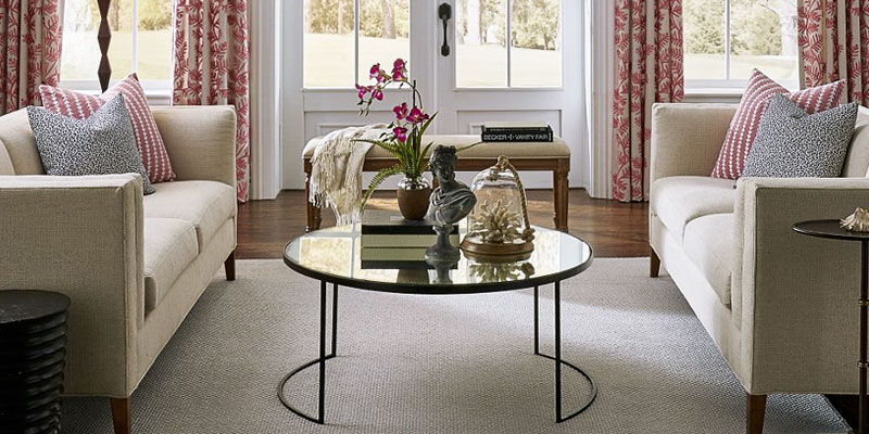 how to choose an area rug- a minimalist, sturdy rug under two cream colored loveseats and a round, glass coffee table